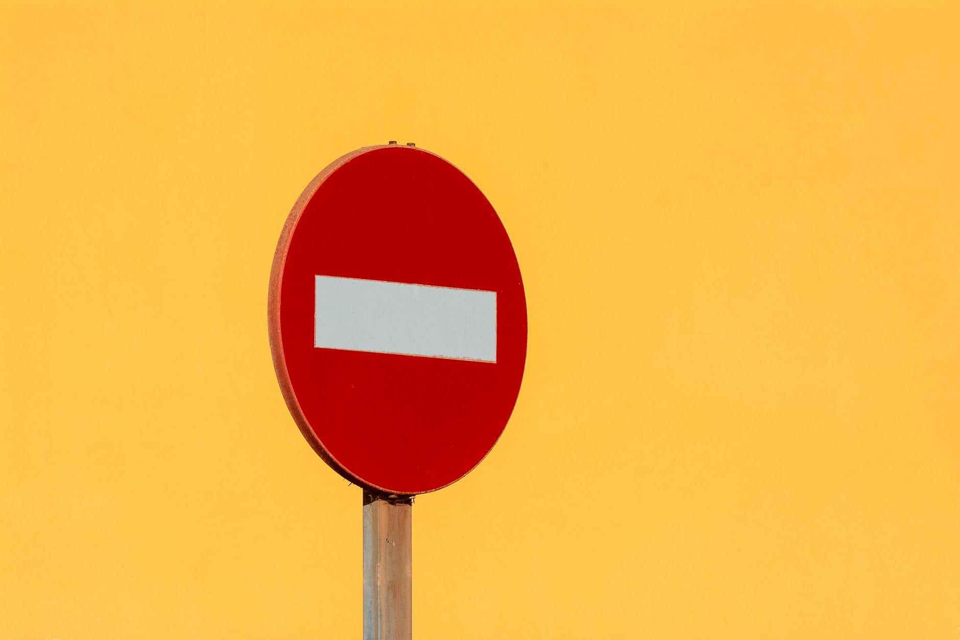 Red no entry sign on pole against bright yellow wall, symbolizing restriction and caution.
