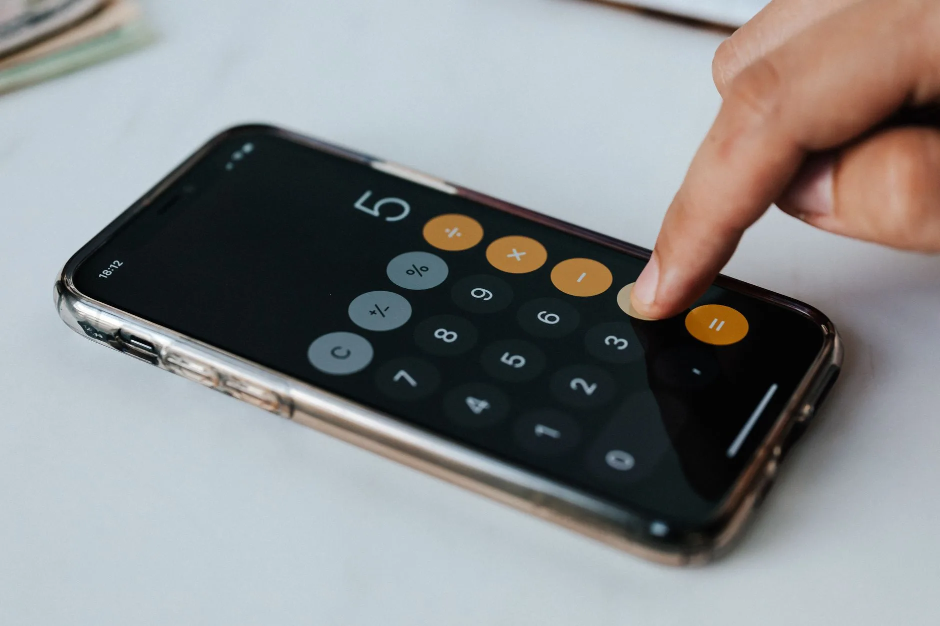 Crop faceless financier touching mobile phone screen during work while calculating on calculator application representing digits and financial symbols